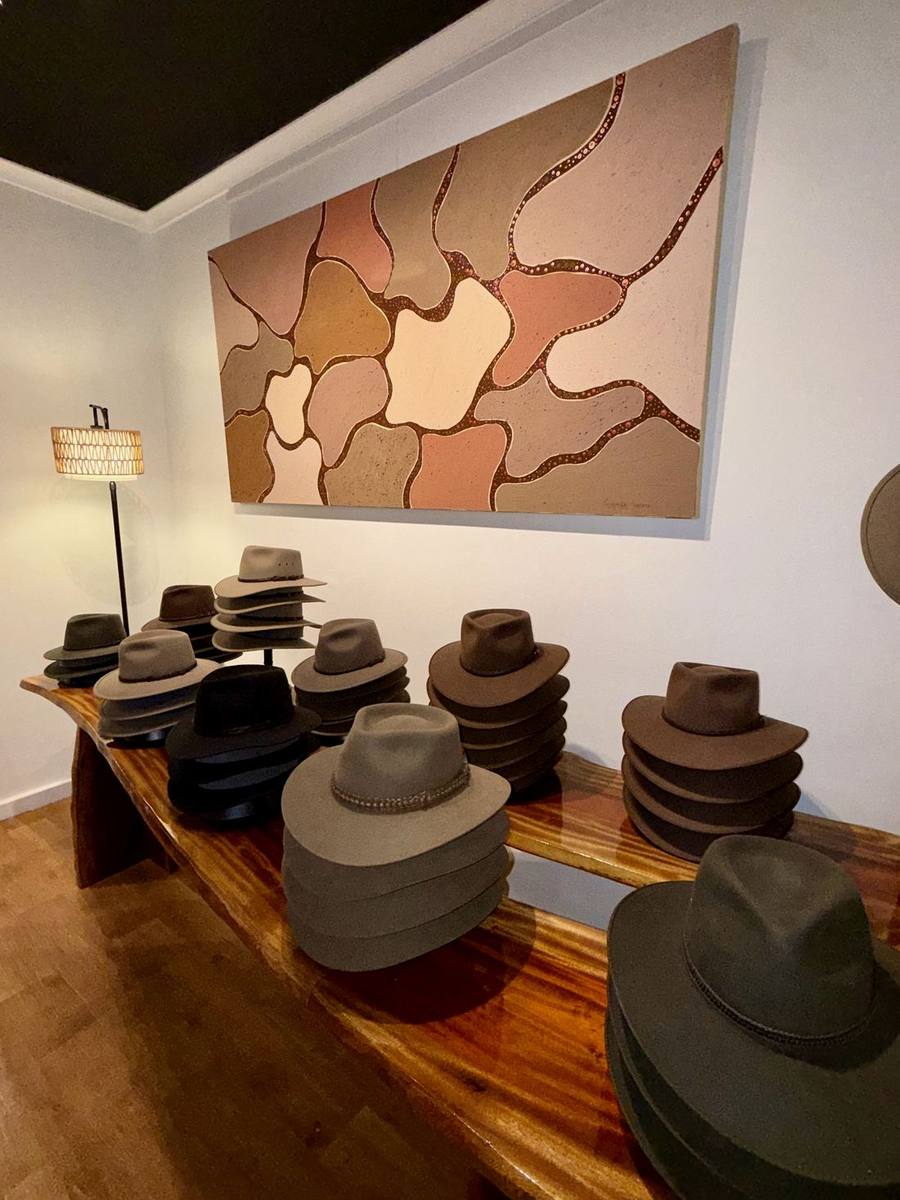 Akubra hats stacked along the live-edge mahogany bench inside The Kimberley Shop, beneath an original canvas.