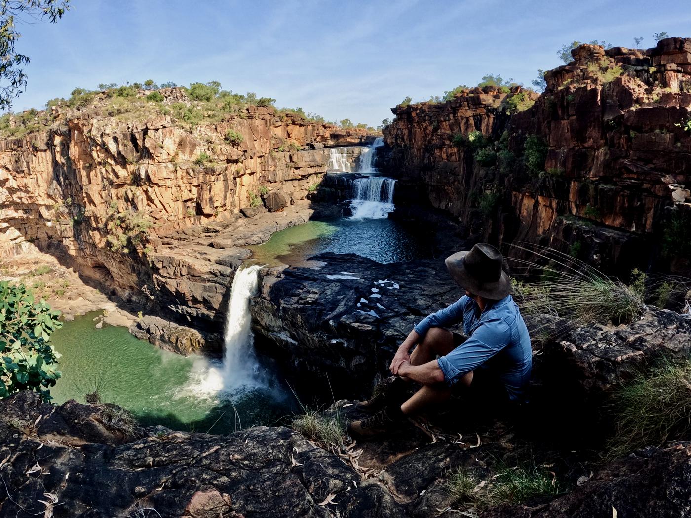 A man in an Akubra sitting above the tiered falls and green pools of Mitchell Falls in the north Kimberley.