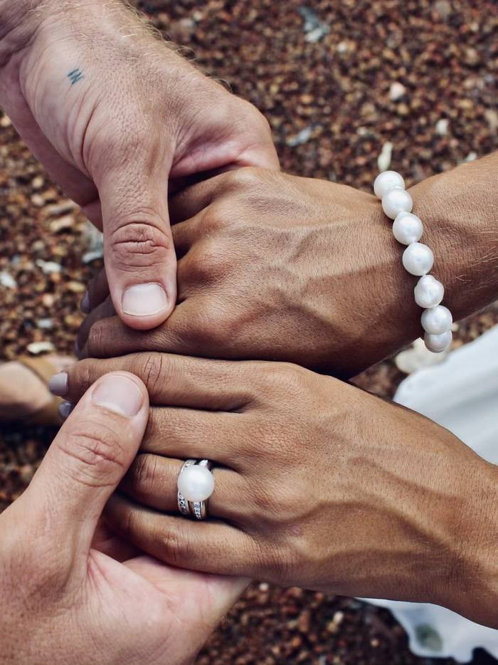 A pearl strand bracelet and a pearl ring worn on joined hands.